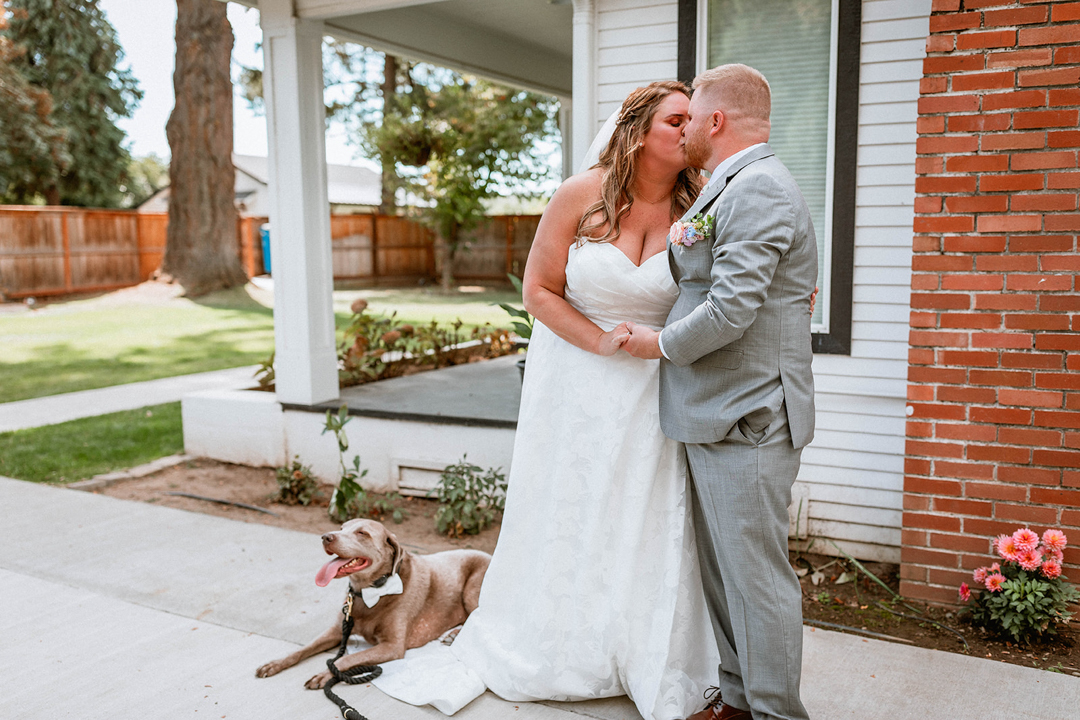 Bride and Groom Kiss at A River House while their Dog looks on